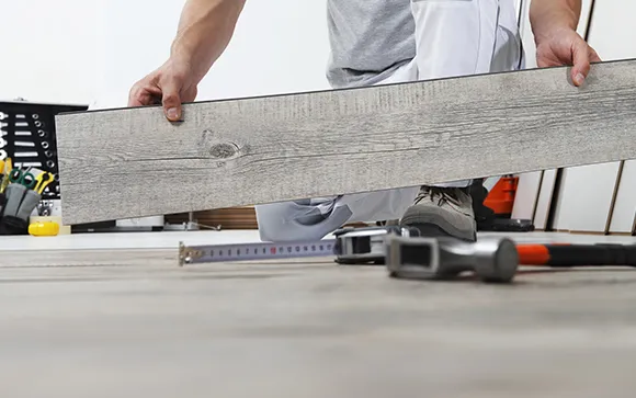 Close-up of hands installing luxury vinyl plank flooring resembling wood texture in Troy MI.