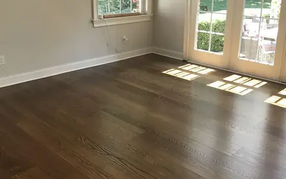 Empty room showcasing dark laminate wood flooring and natural light from windows.