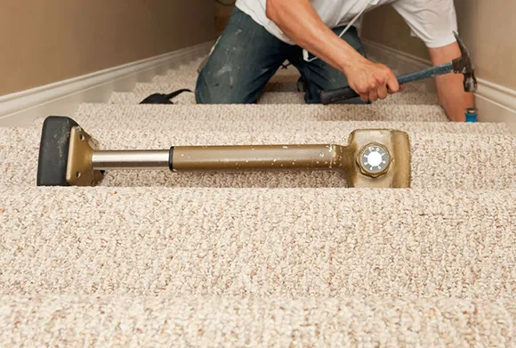 Worker installing beige carpet on stairs using knee kicker tool for stair carpet installation in Saline MI.