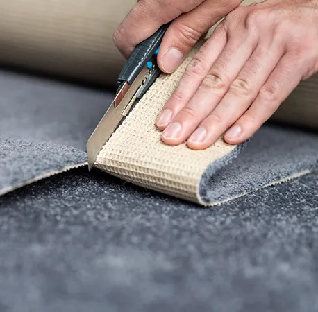 Close-up of hands using a knee kicker tool to stretch and secure carpet edges during installation.