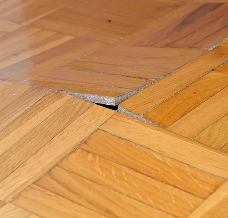 Close-up of damaged parquet wood flooring with visible cracks and warping needing repair.