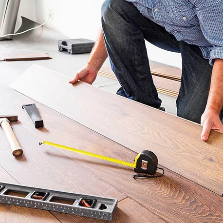 Close-up of carpenter measuring and cutting hardwood flooring with tools on wooden surface.