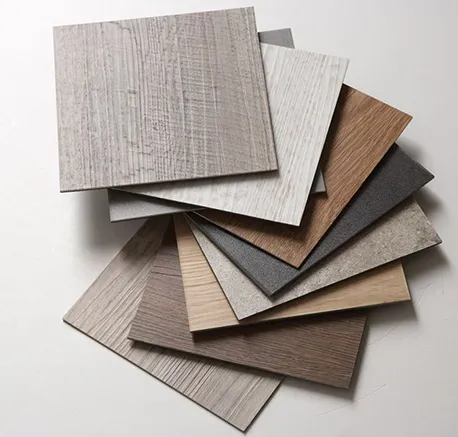 Stack of luxury vinyl plank (LVP) flooring samples showing various wood textures and shades on a neutral background.