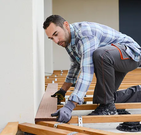 Installer kneeling and using tool to fit floorboard tightly for same-day flooring installation.