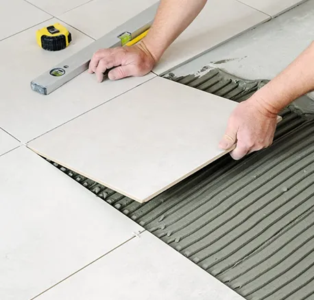 Hands installing large white ceramic tiles with adhesive on floor during ceramic tile repair.