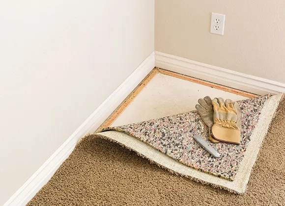 Corner of room with beige carpet partially rolled back exposing subfloor during installation.