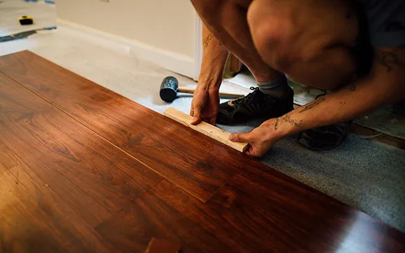 Close-up of a flooring installer using a tool to fit hardwood planks during floor installation.