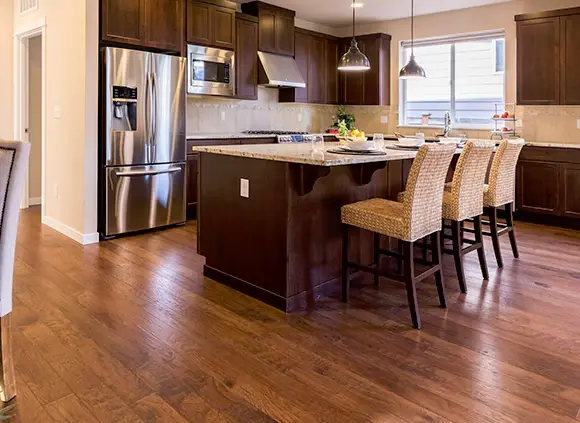 Modern kitchen with dark wood laminate flooring, granite countertop island, stainless steel appliances, and high wicker bar stools.
