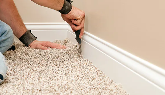 Close-up of professional trimming carpet edges with a carpet knife for clean installation.