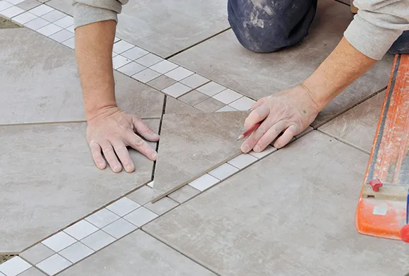 Close-up of hands installing ceramic tiles during floor renovation.