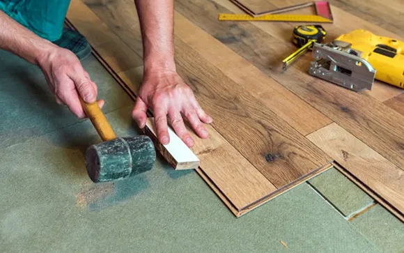 Hands sanding hardwood floor boards during refinishing process.
