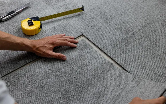 Close-up of worker measuring carpet flooring with tape measure.
