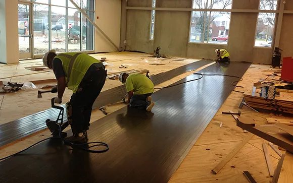 Professional installers fitting hardwood flooring planks in spacious West Bloomfield MI living room.