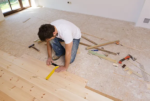 Professional installer measuring and laying wooden floor planks in Ann Arbor MI home.