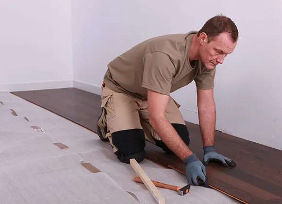 Professional installer kneeling and laying laminate flooring planks with tools in Troy MI.