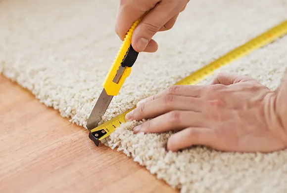 Close-up of carpet repair showing hands using utility knife to fix worn edge in Canton MI.
