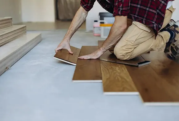 Technician installing hardwood floor planks on living room subfloor.