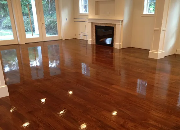 Shiny polished hardwood flooring in a room with a fireplace and large windows.