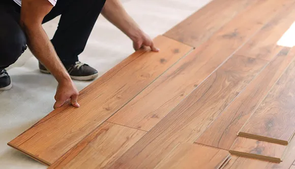 Person laying and aligning hardwood flooring planks during professional hardwood floor installation.