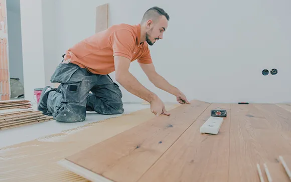 Flooring installer fitting hardwood floor planks in home interior.