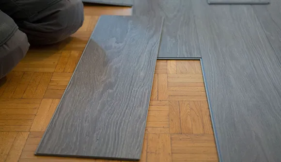 Hands installing dark luxury vinyl plank flooring over a wooden subfloor in Madison Heights.