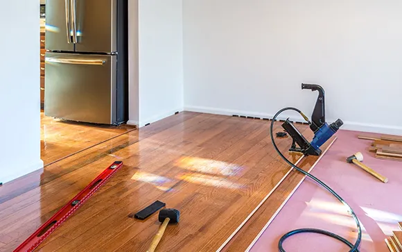 Laminate flooring installation in progress with tools and unfinished floor panels in a residential setting.