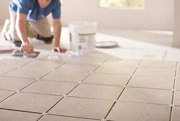 Close-up of a professional using a trowel to apply grout between newly installed ceramic floor tiles.
