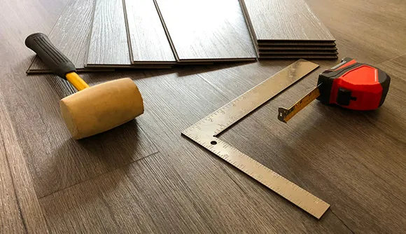 Square, measuring tape, and hammer placed on wooden luxury vinyl plank flooring for precise installation.