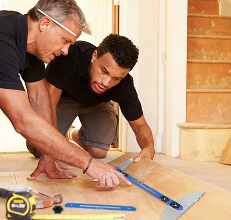 Two flooring specialists measuring and fitting wooden floor planks during installation.